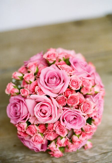 A tightly arranged floral bouquet consisting predominantly of soft pink roses and smaller pink buds, with green foliage peeking through. The roses display lush, velvety petals in full bloom, creating