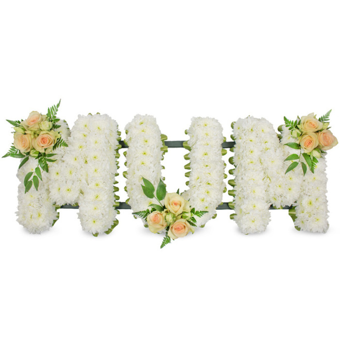 A tasteful and heartfelt floral tribute spelling out "MOM" is displayed here against a clean, bright white background, allowing the careful detail of the design to take centre stage. Each of the three capital letters is completely filled with compact white chrysanthemums or similar small blooms, arranged tightly together so that the petals form a soft, billowing surface reminiscent of freshly fallen snow. The flowers are fresh and luminous, their creamy white tones reflecting light in a way that feels serene and comforting, like a calm morning over the nearby River Thames at Leamouth. Around the outer edges of each letter, a slim green border of ribbon and foliage provides definition, gently contouring the shapes and giving the word a well-structured, finished look. The cool white base is gently warmed by three carefully positioned accents of peach and apricot roses. One floral cluster sits at the upper left of the first "M", another nestles at the lower centre of the "O", and the final cluster graces the top right of the last "M", balancing the design from side to side. Each cluster includes both open roses and tighter buds, surrounded by bright green leaves and delicate fern fronds that introduce texture and a soft sense of movement. The interplay between the velvety rose petals and the daisy-like chrysanthemums creates visual interest while retaining a respectful, understated feel. This floral lettering arrangement is clearly designed as a personal memorial for a much-loved mother, an appropriate choice for a funeral or cremation service in the Leamouth area, where families might wish to express enduring love, remembrance, and gratitude with flowers that feel both contemporary and deeply sincere.